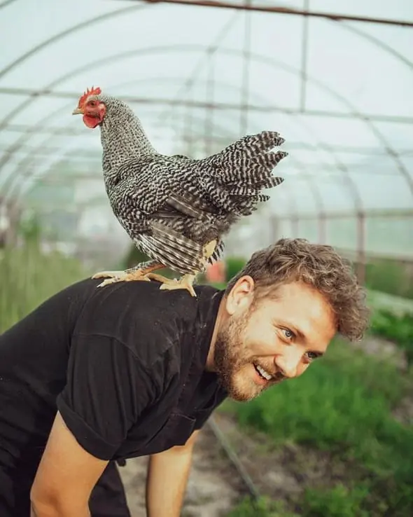 Alex Iacob zâmbind, cu o găină pe umăr, într-un solar