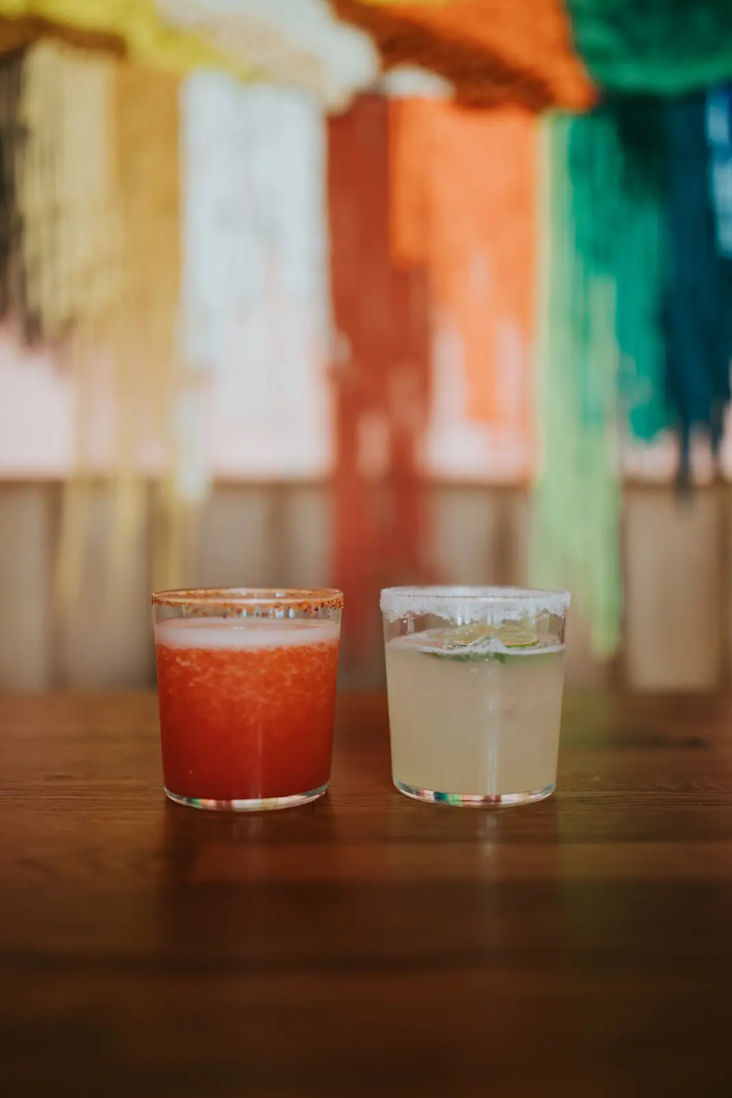 Două margarita cu buza de sare și chili, pe o masă de lemn, cu textile mexicane în spate